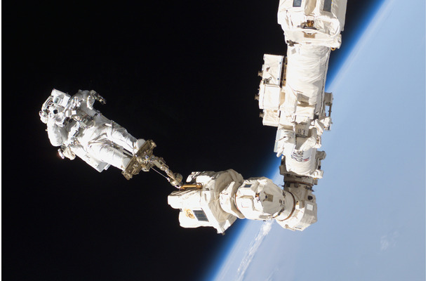 国際宇宙ステーションのロボットアームに足を固定して、ニコンの機材で撮影するロビンソン宇宙飛行士